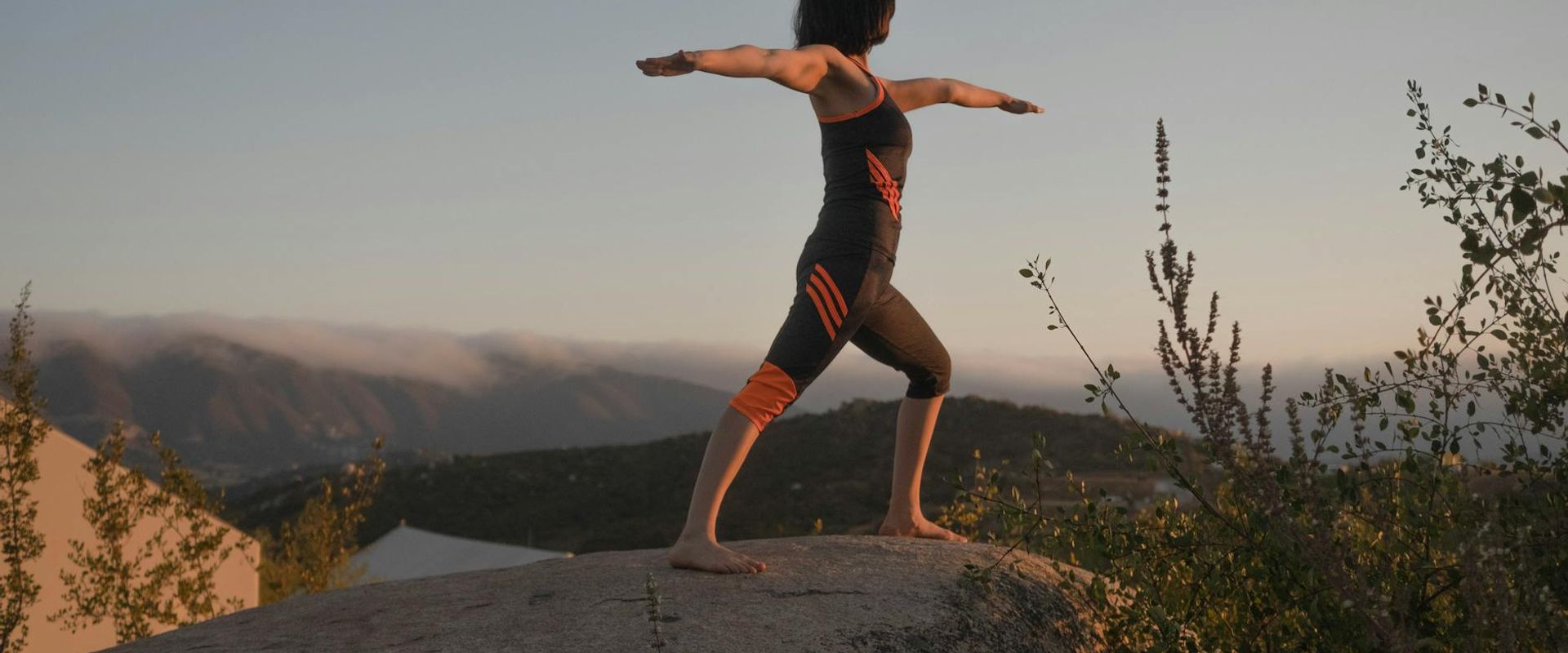 Woman meditating in a serene outdoor yoga pose at sunset.